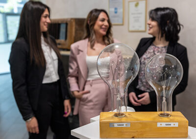 Immagine di tre ragazze sorridenti. In rimo piano, duelampadine.